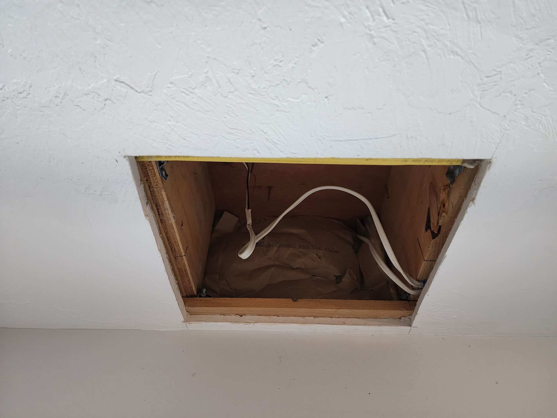 Open ceiling electrical box with exposed white wiring in a white wall.