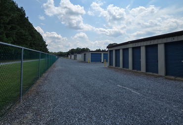 Gravel path beside blue storage units and a chain-link fence under a cloudy sky