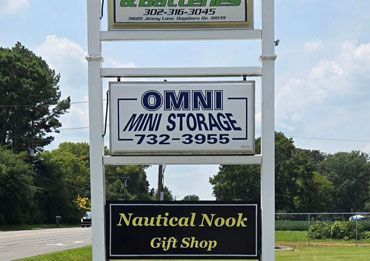 Roadside sign for Omni Mini Storage and Nautical Nook Gift Shop against a green, tree-lined background