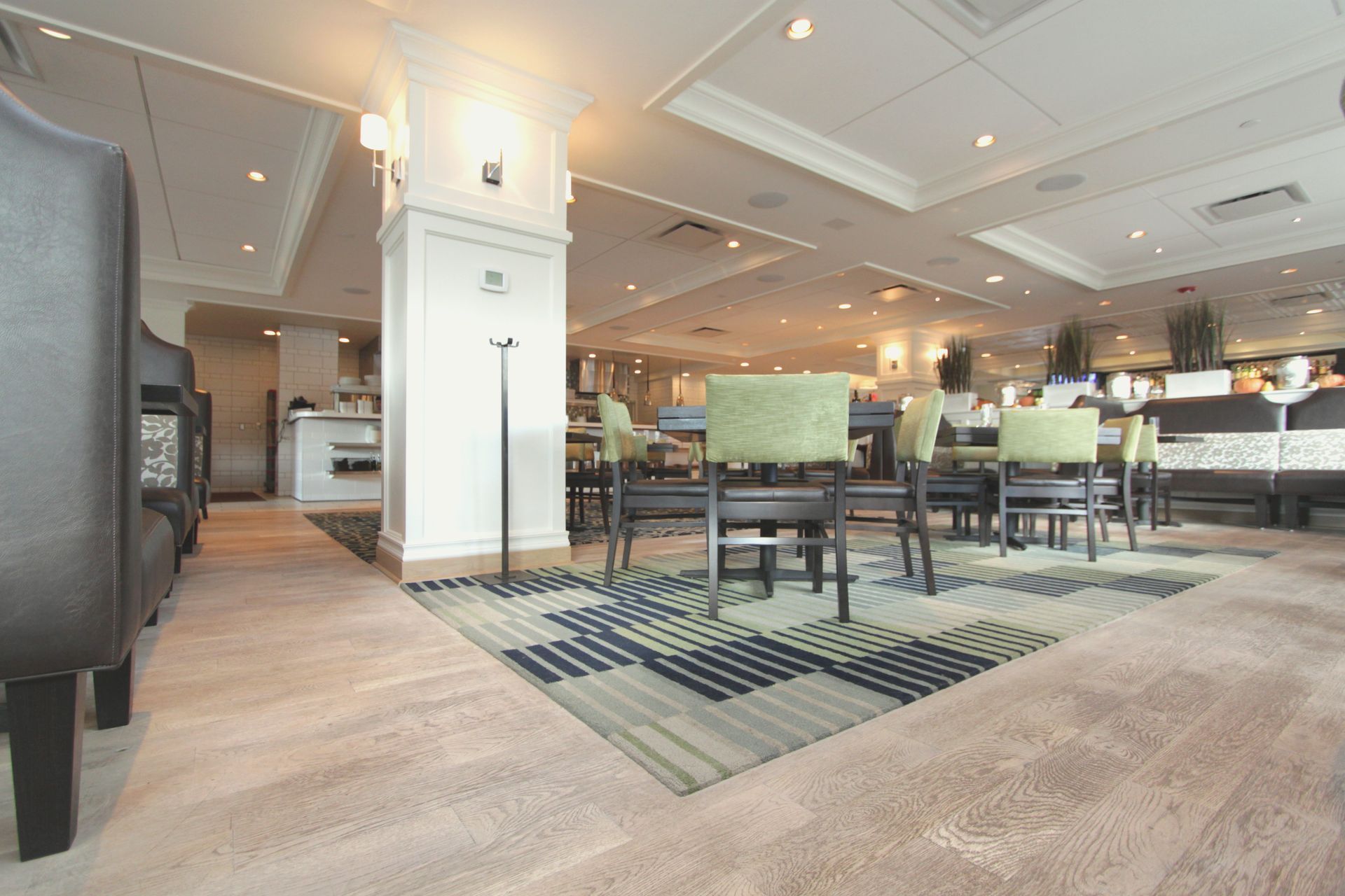 Restaurant interior with tables and chairs on patterned rug, neutral walls.