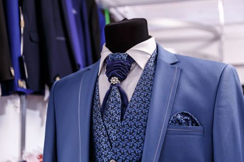 Blue suit jacket with patterned vest, tie, and pocket square on a mannequin in a clothing store.