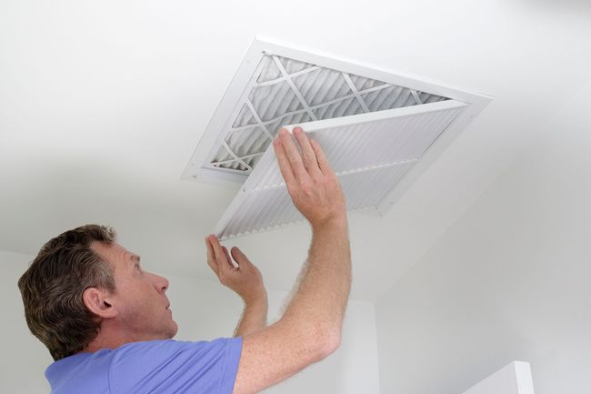 Man replacing an air filter in a ceiling vent. White room, hands holding new filter.