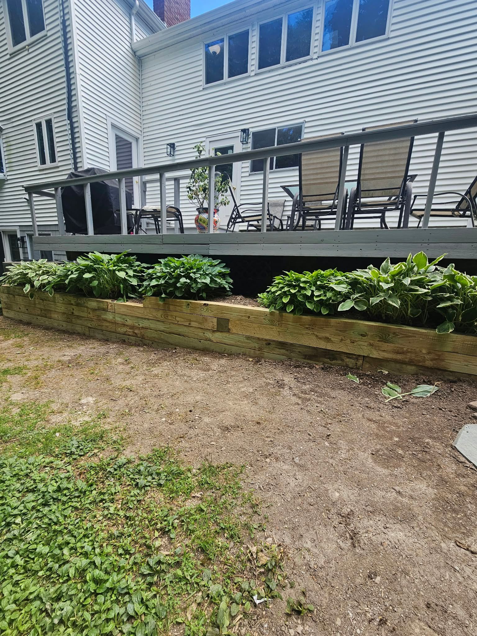 Backyard deck with black railing, green shrubs, and a beige house exterior.