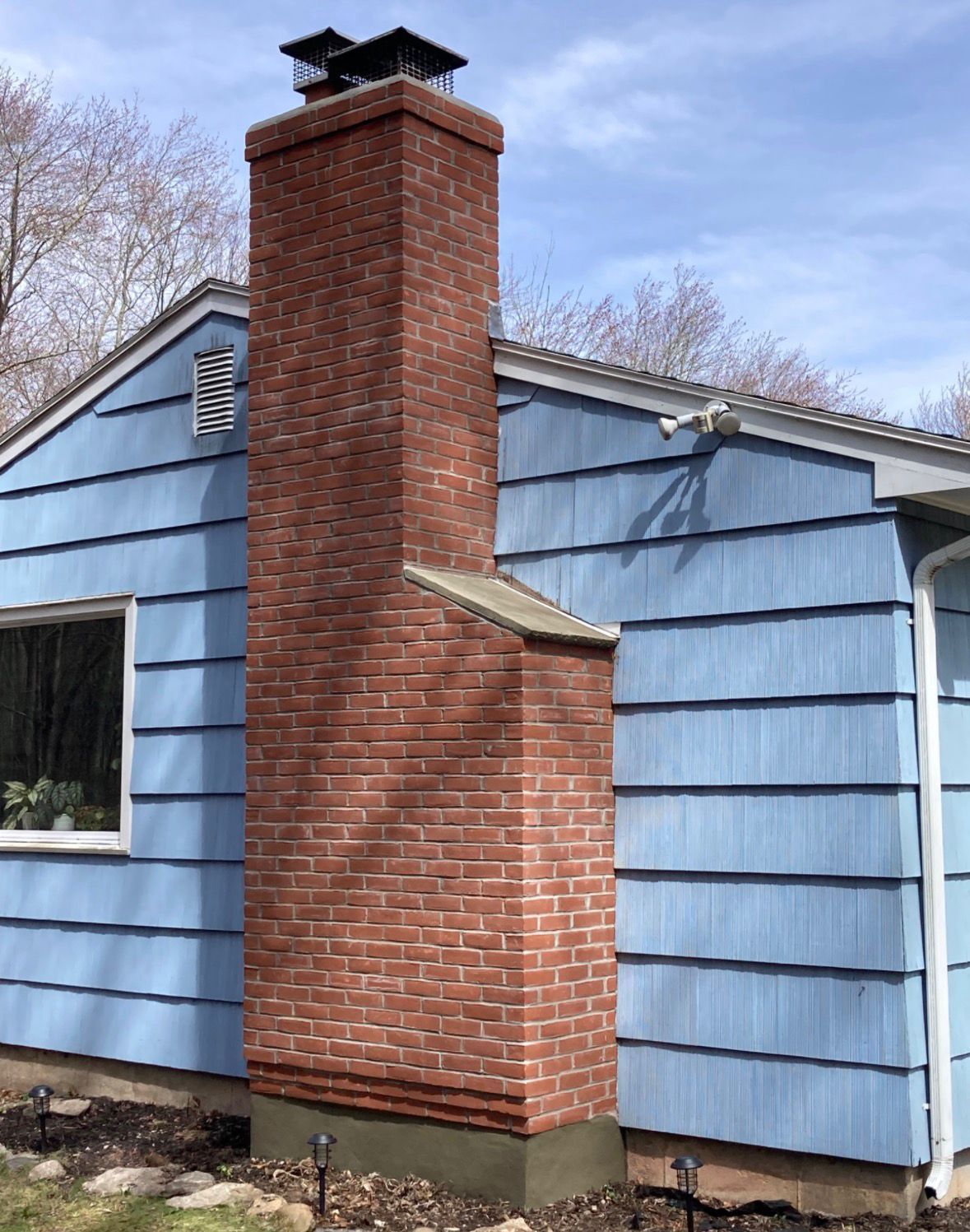Brick chimney attached to a blue house with a black cap on top
