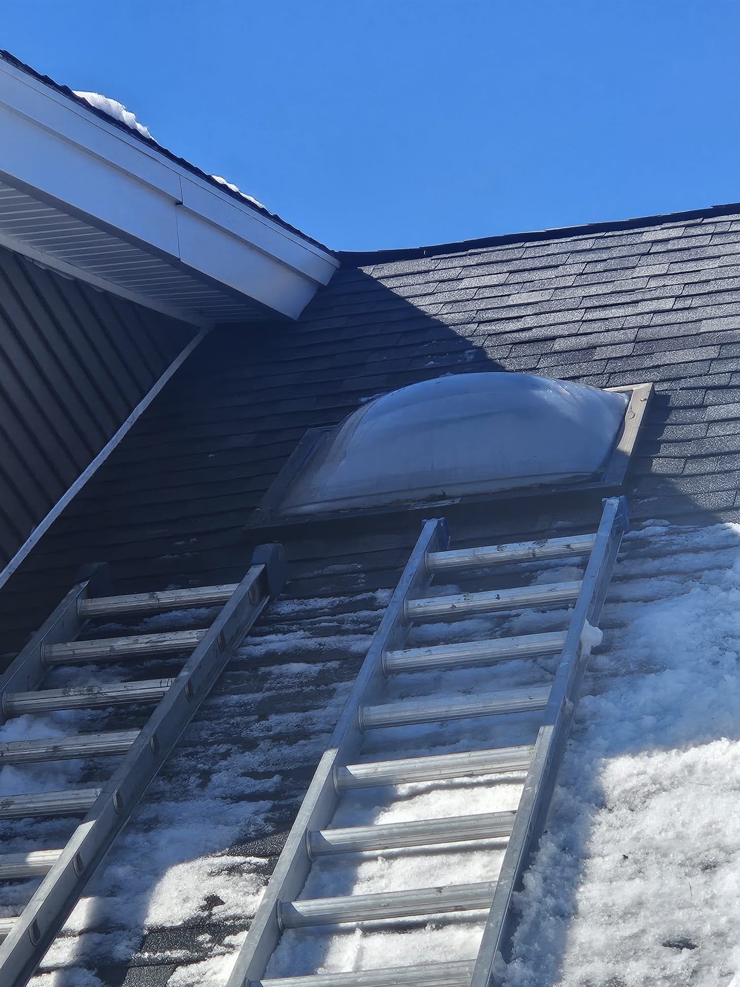 Two ladders leaning against a house roof near a dormer under a blue sky