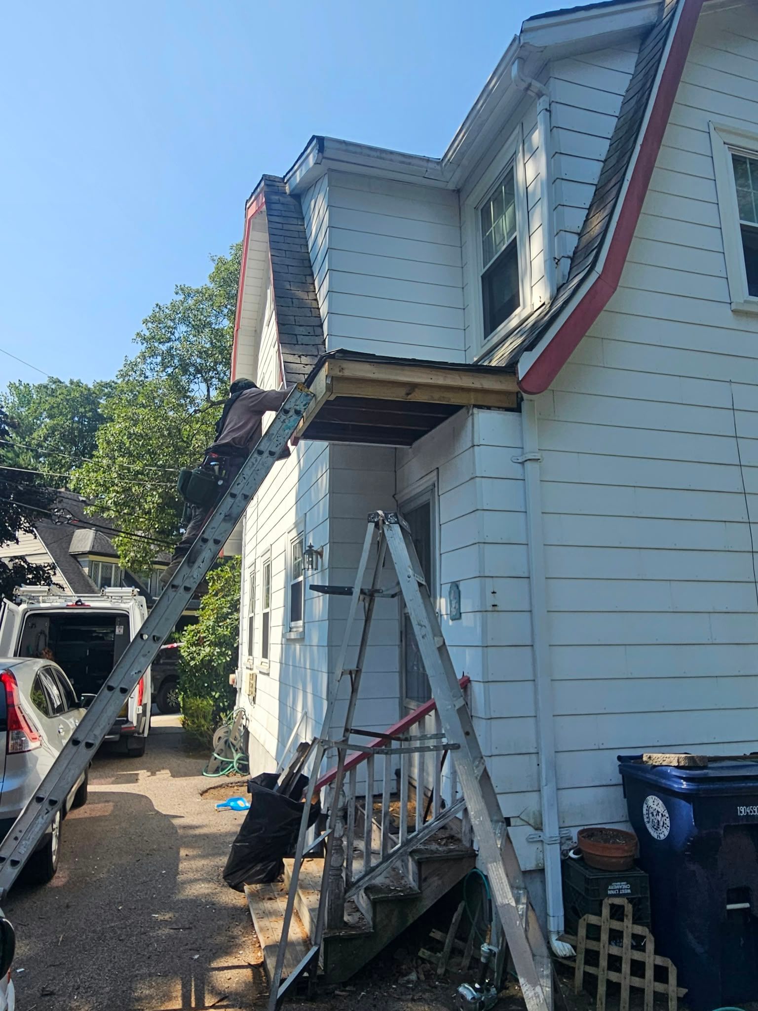 Two-story house with white siding under repair, with scaffolding and a ladder beside the porch.