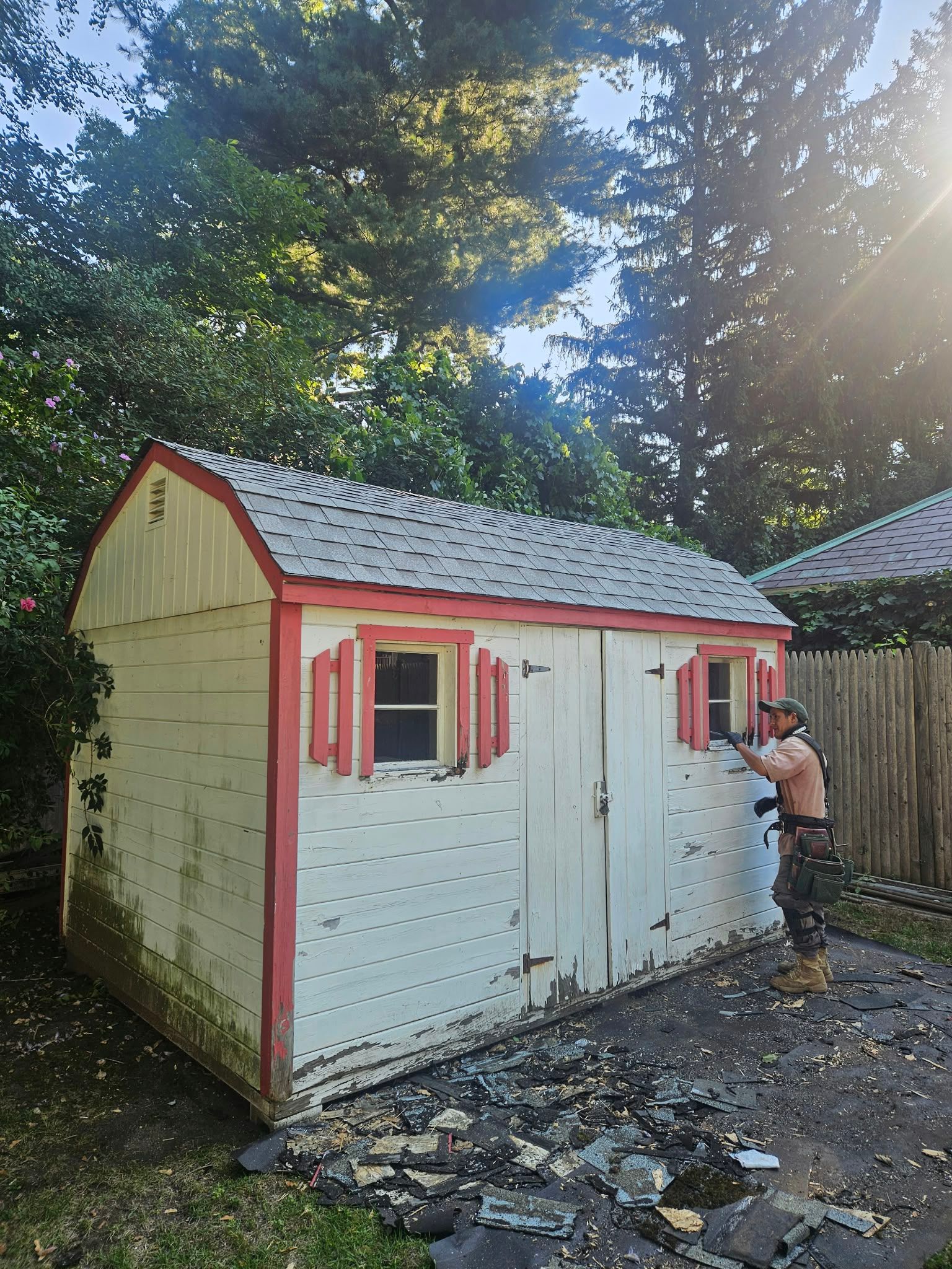 Small white shed with red trim in a wooded yard; a person stands by the door.