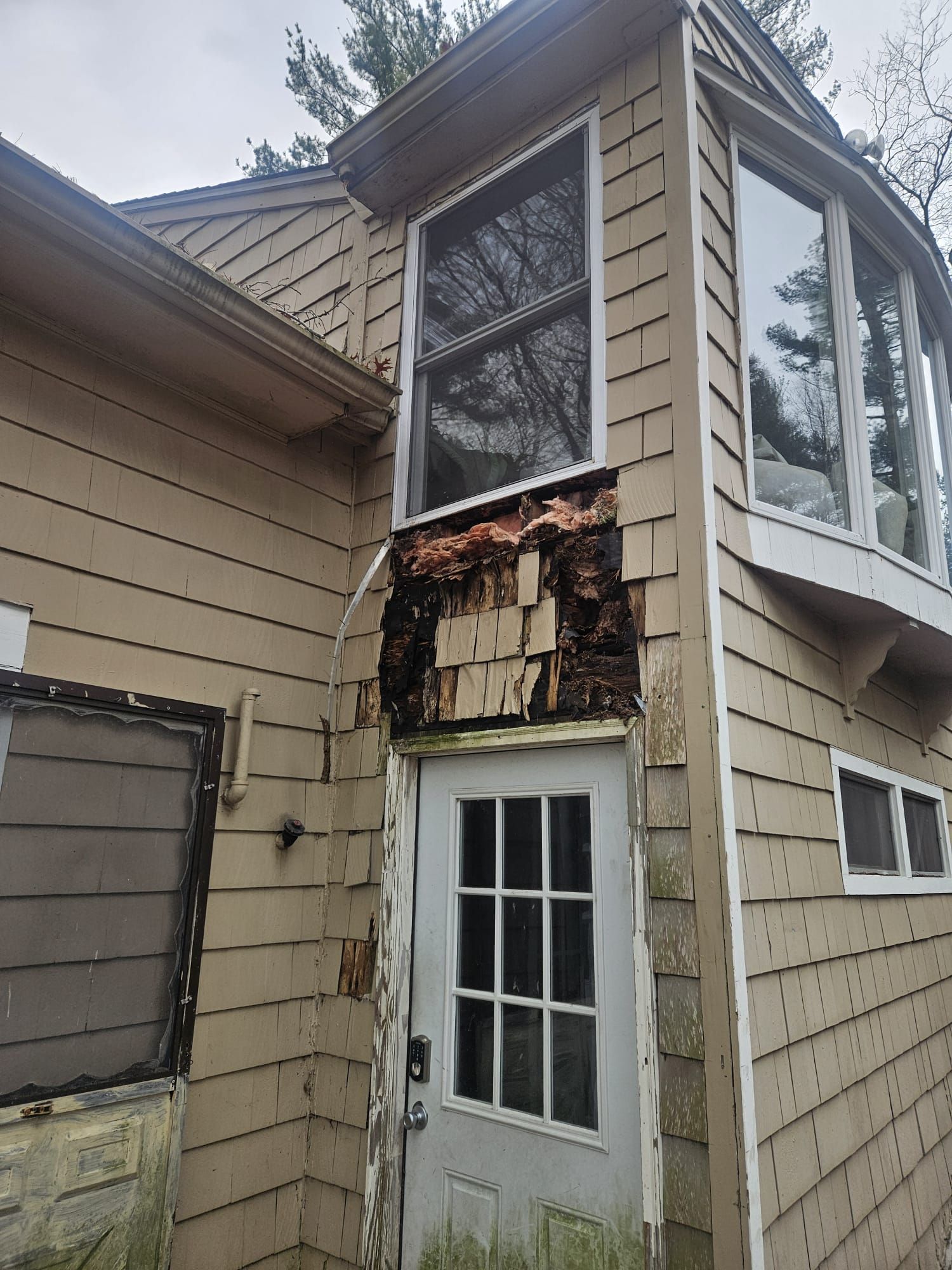 Damaged exterior wall with exposed insulation above a white door on a beige house