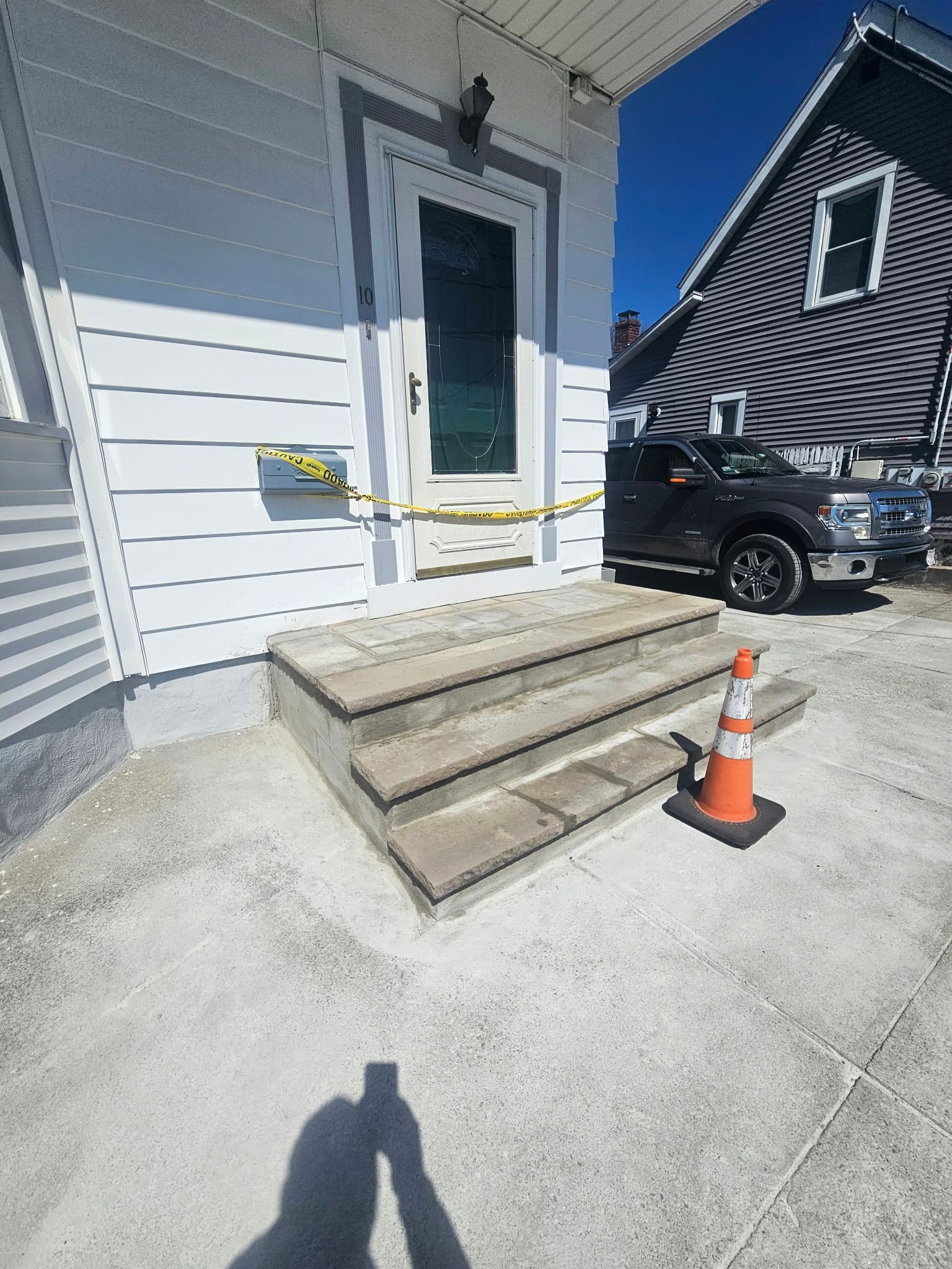 House entrance with concrete steps taped off by caution tape, next to a parked black truck and orange cone.