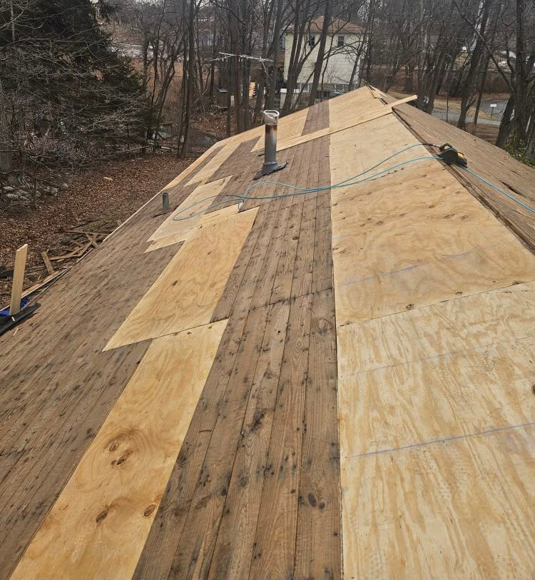 Roof under repair with plywood patches and a chimney on a wooded hillside.