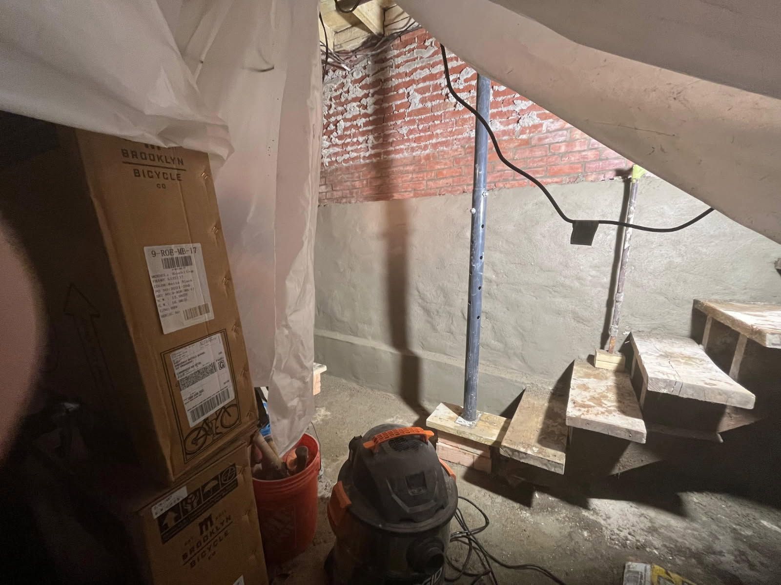 Construction area with stairs, brick wall, cardboard boxes, and tools under a tented covering