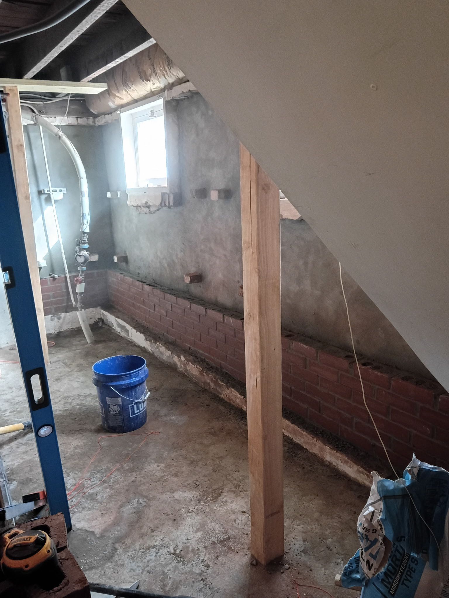 Unfinished room with exposed walls, a wooden support post, blue bucket, and debris on the floor
