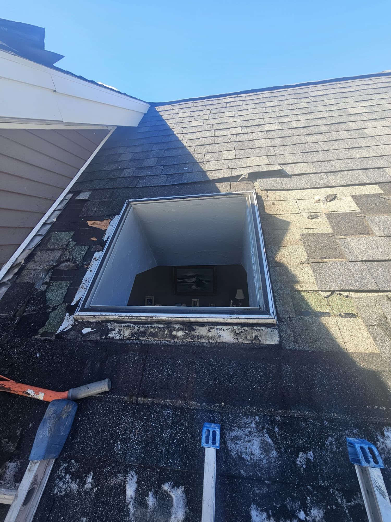 Open roof hatch on a shingled roof, with surrounding vents and tools near the edge.