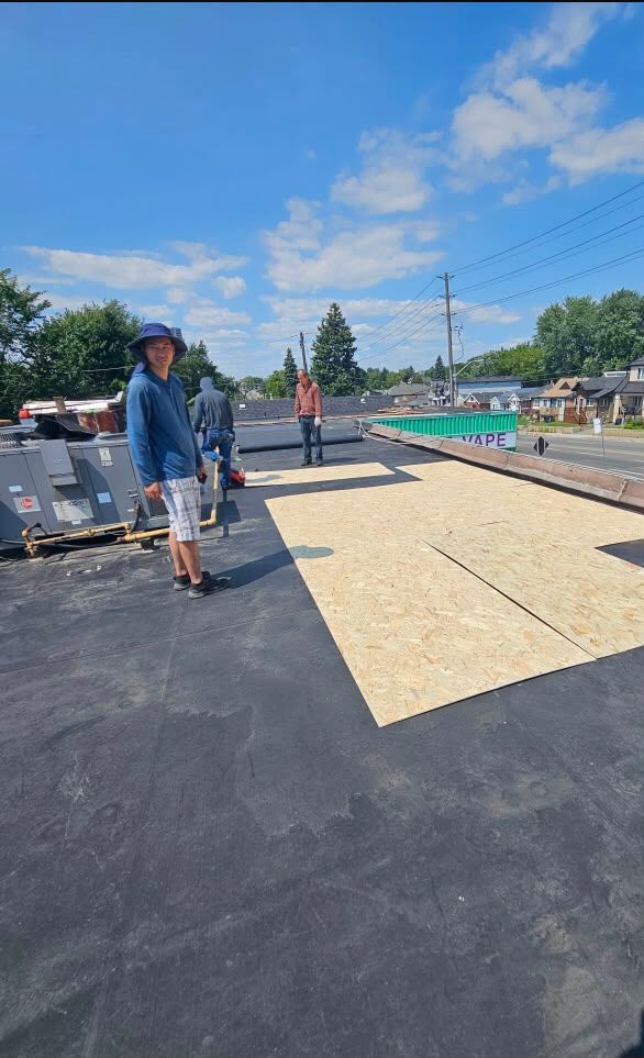 Workers installing roofing felt on a flat roof under a bright blue sky