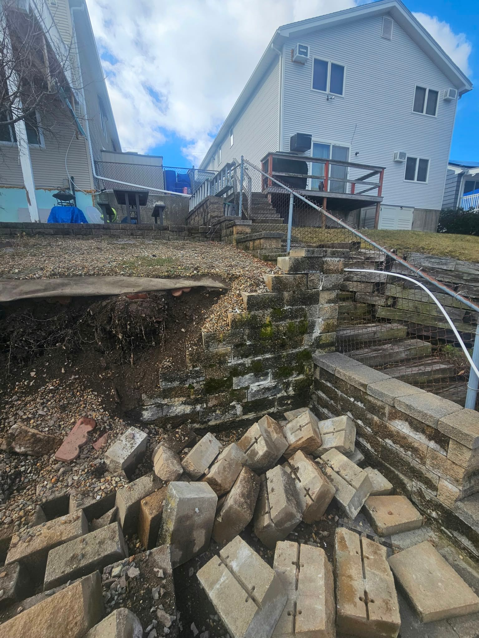 Collapsed retaining wall with broken concrete blocks and a house above on a hillside