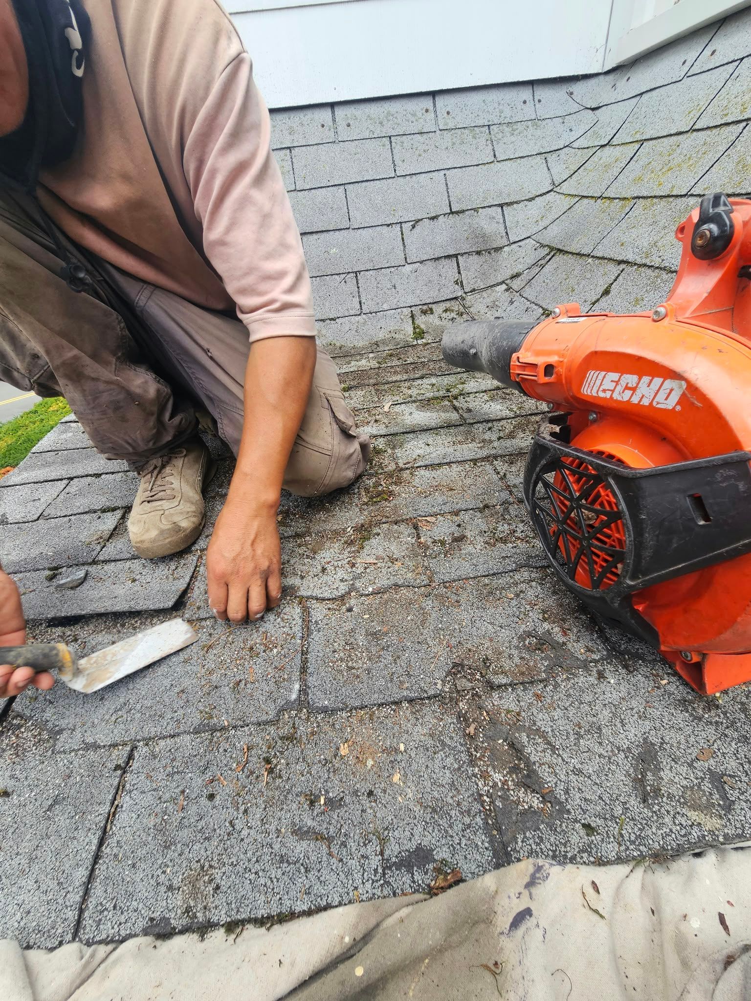 Worker installing gray roof shingles beside an orange saw on a rooftop