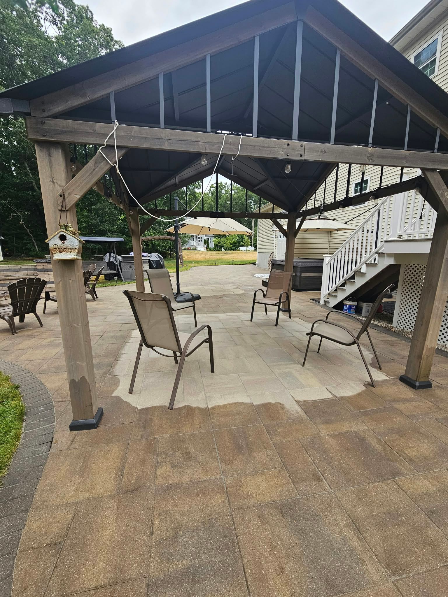 Covered outdoor patio with chairs, a wooden play structure, and a stone floor in a yard