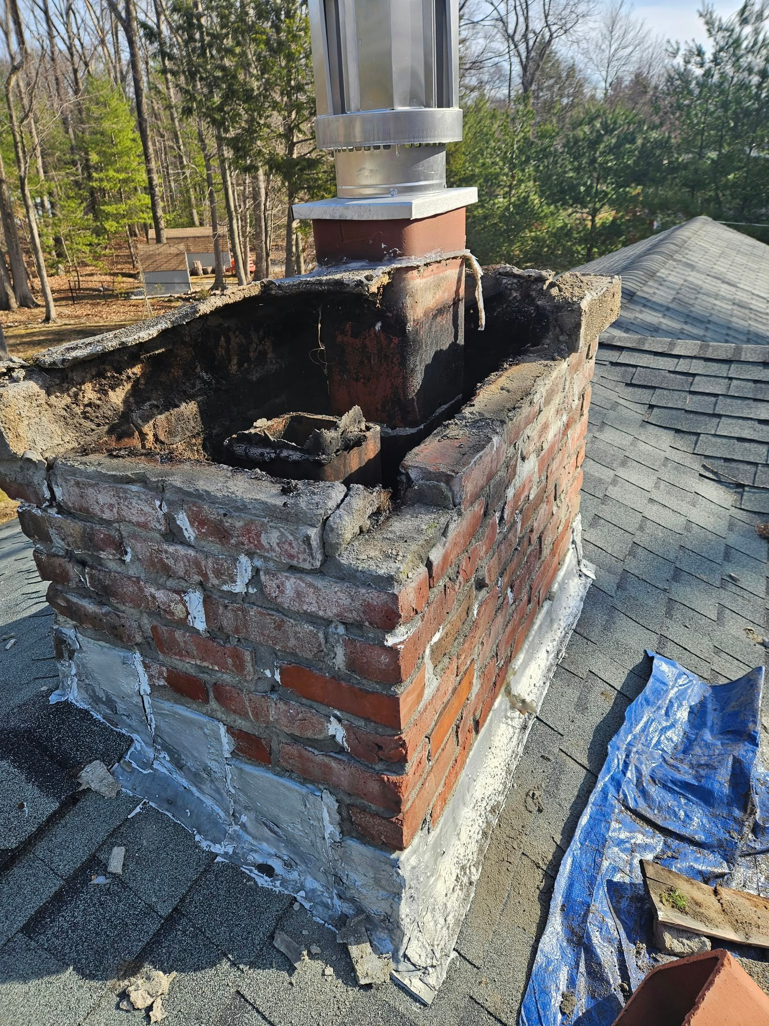 Damaged brick chimney with a charred opening on a rooftop, with roofing debris nearby