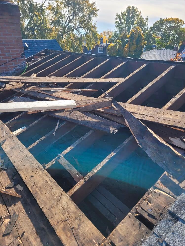 Collapsed wooden roof with exposed beams and blue sky visible through the damage