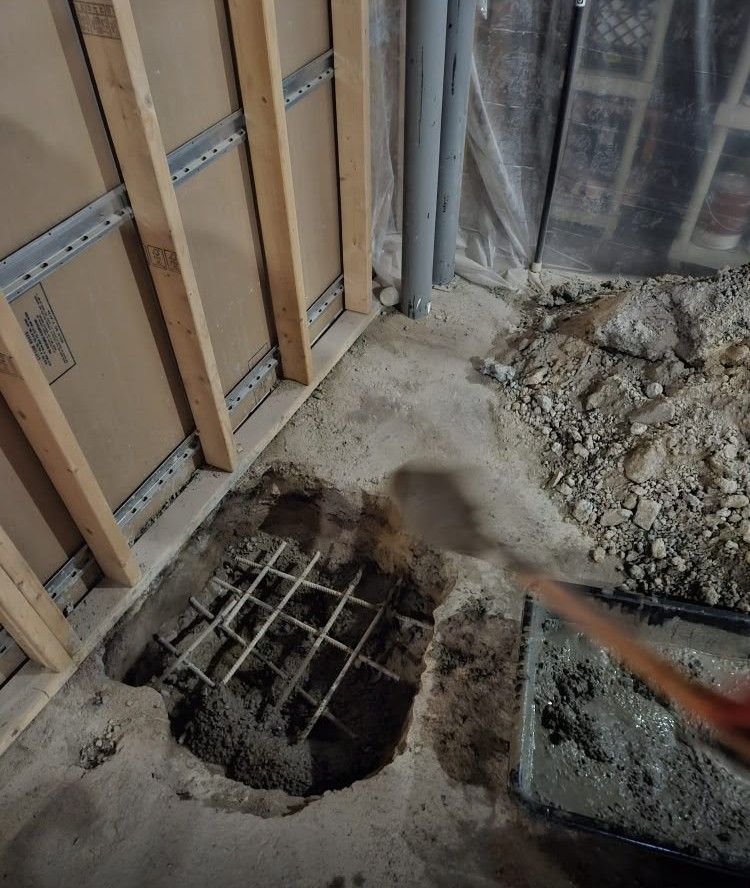 Construction site floor cutout with exposed rebar, framing studs, debris, and a trowel nearby