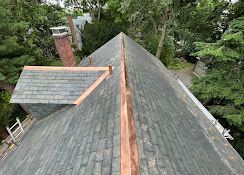 Roofing ridge with gray shingles and copper flashing, viewed from above with trees surrounding the house