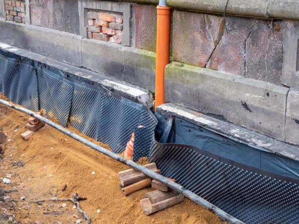 Construction site trench with black drainage mesh along a stone wall and orange pipe support