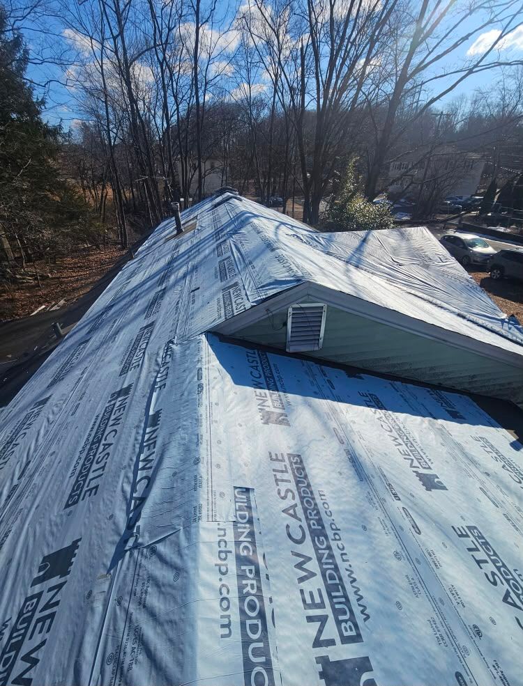 Roof under construction with new synthetic underlayment and a dormer, viewed in a wooded area
