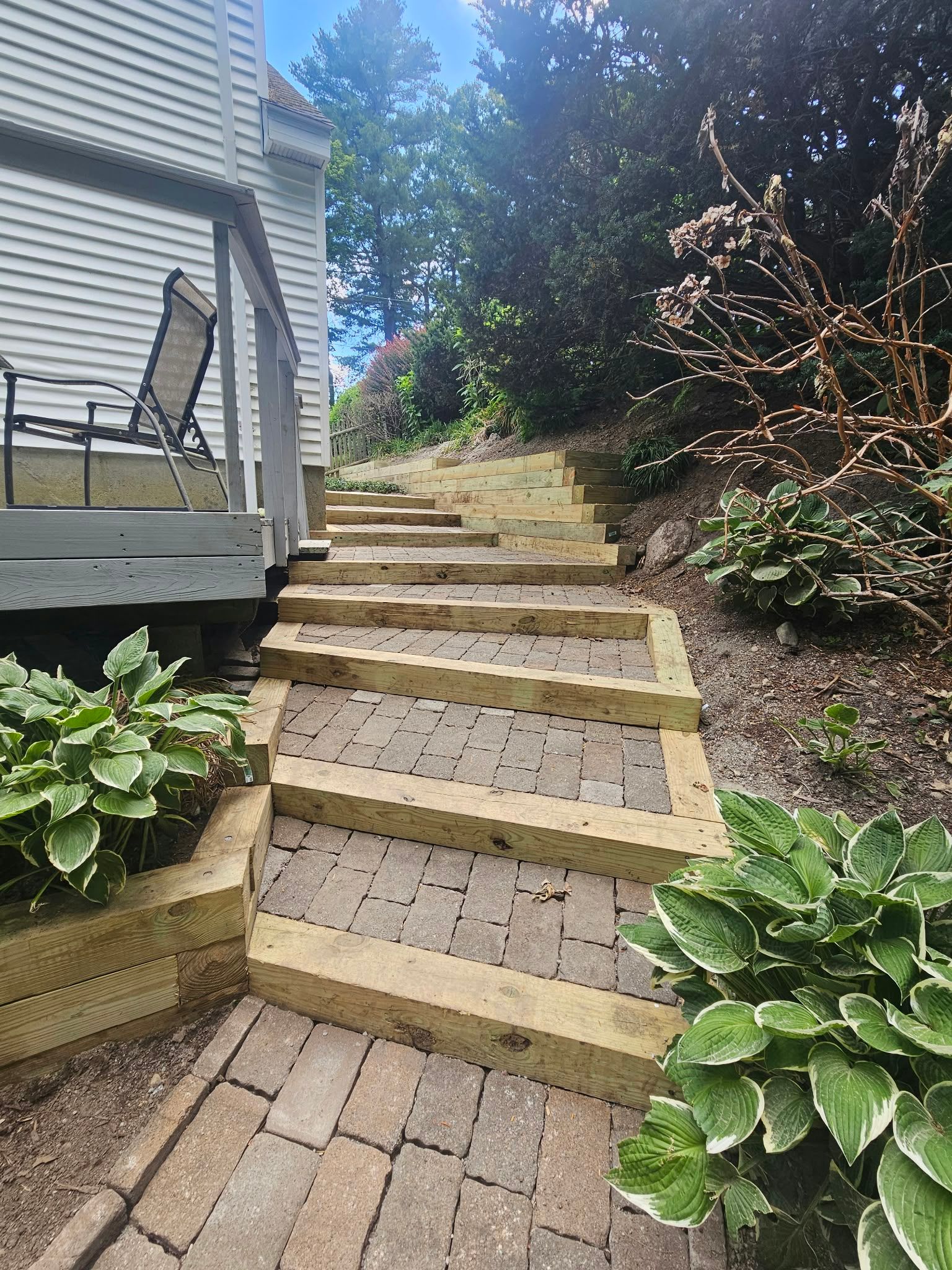 Steep outdoor brick steps beside a house, lined with tan timbers and lush green plants.
