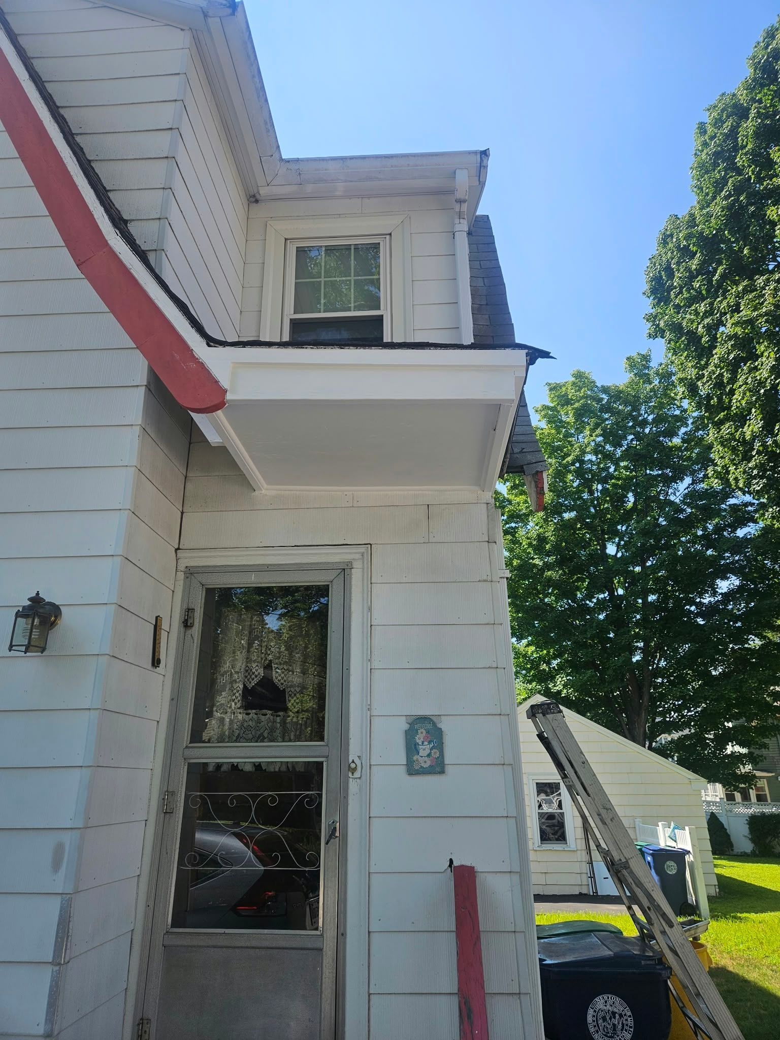 White house exterior with red trim, upper window, and a ladder leaning beside the side wall.