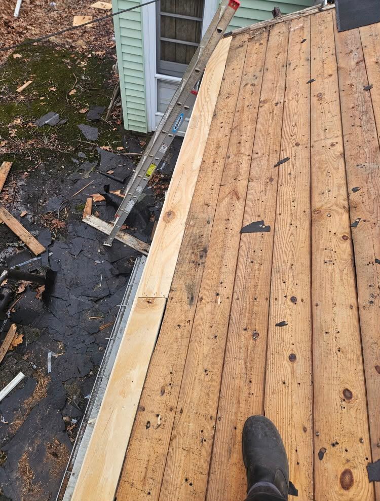 Rooftop under repair with fresh plywood sheathing and scattered debris along the edge.