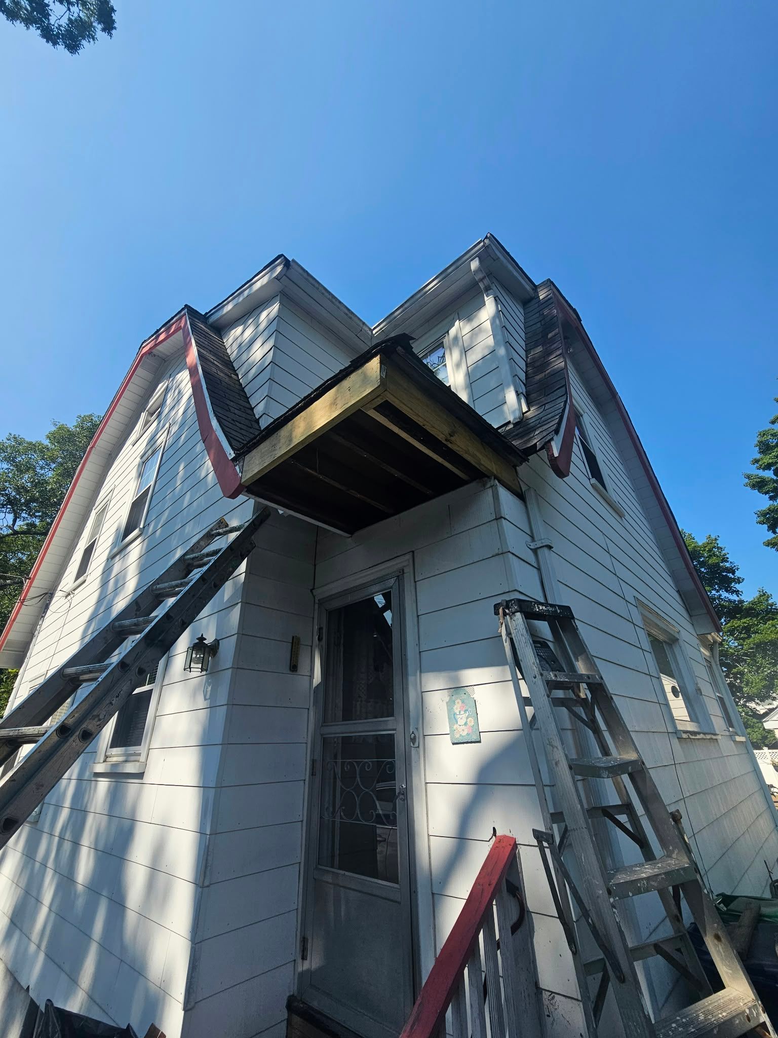 Small white house with steep roof and ladders leaning against it under a blue sky