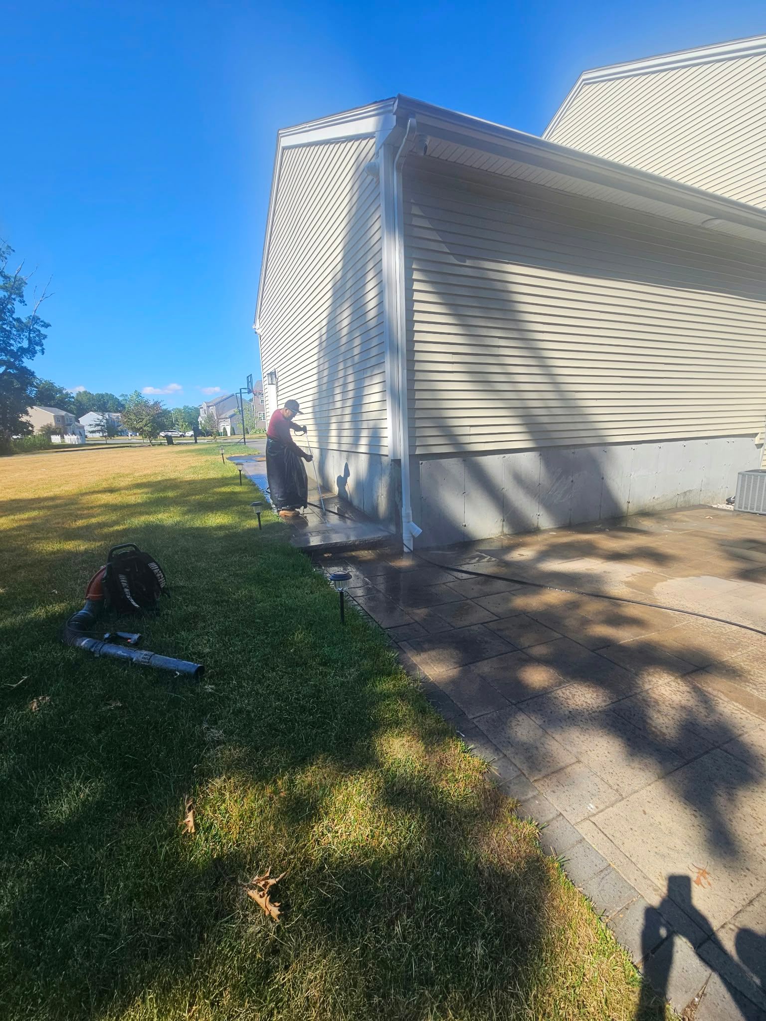 Side of a white house with a person near the wall, grassy yard, and bright blue sky