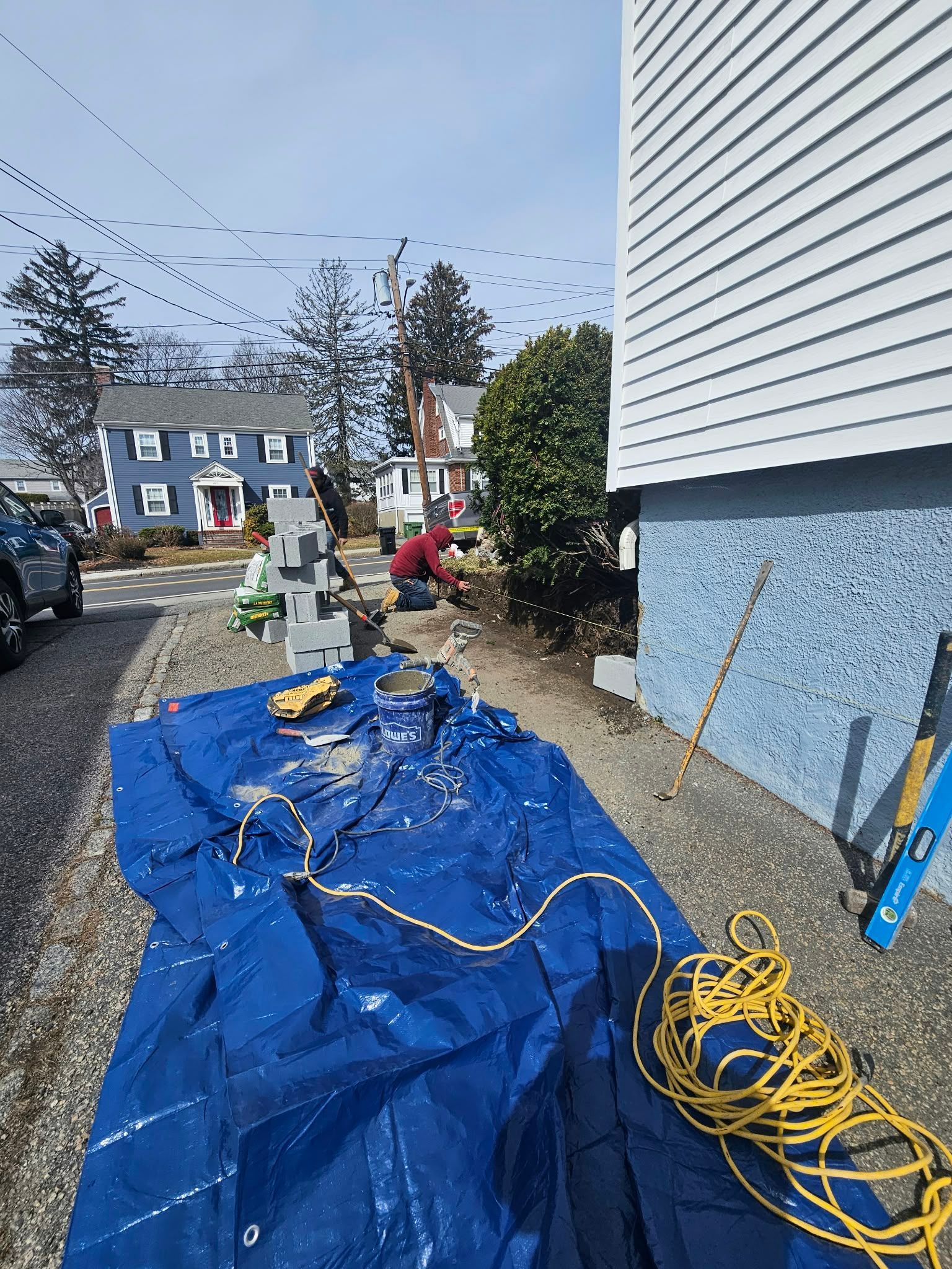 Outdoor work area beside a house with blue tarp, tools, and coiled yellow extension cord.