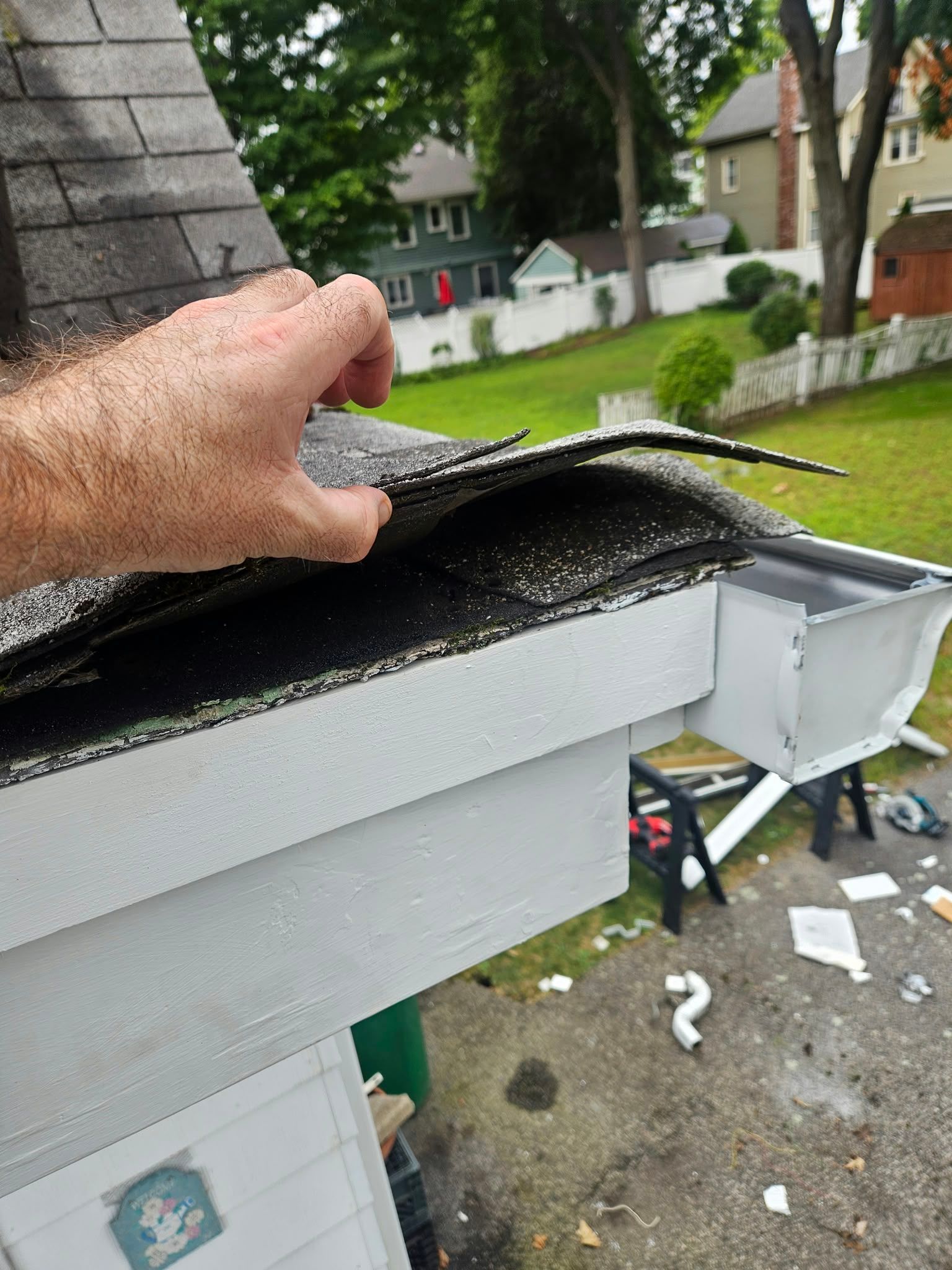 Hand placing roofing felt on a white gutter edge beside shingles and a chimney
