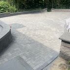 Curved gray stone patio with low walls and greenery in the background