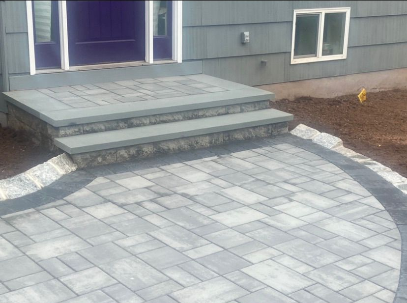 Front steps leading to a gray stone patio beside a house exterior