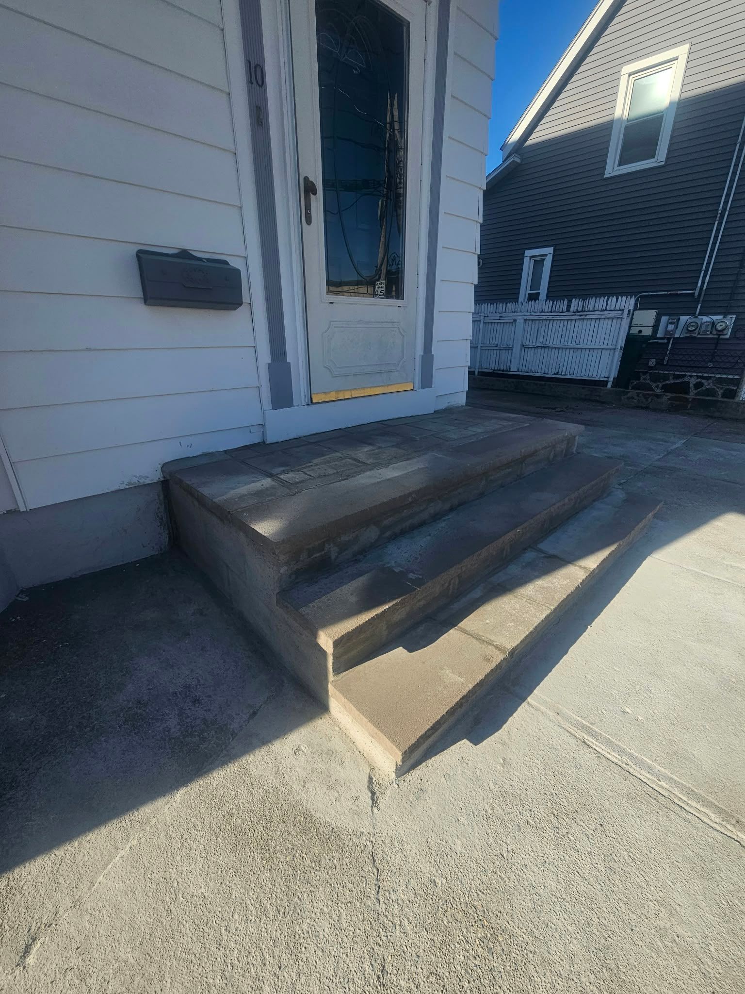 House entry with three concrete steps, a white door, and a black mailbox beside the porch.