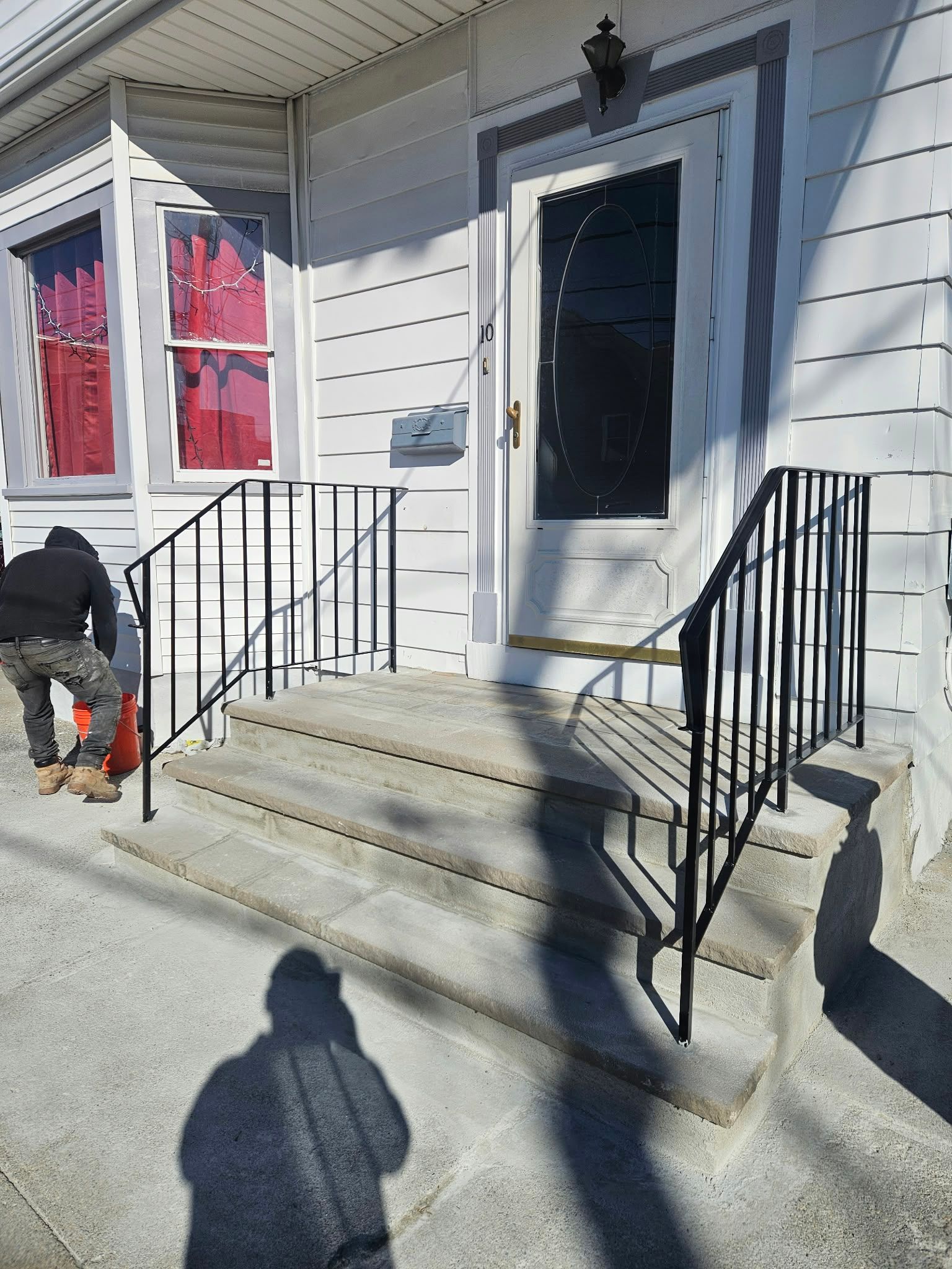 Front porch with white siding, black railings, and a person kneeling near the steps.