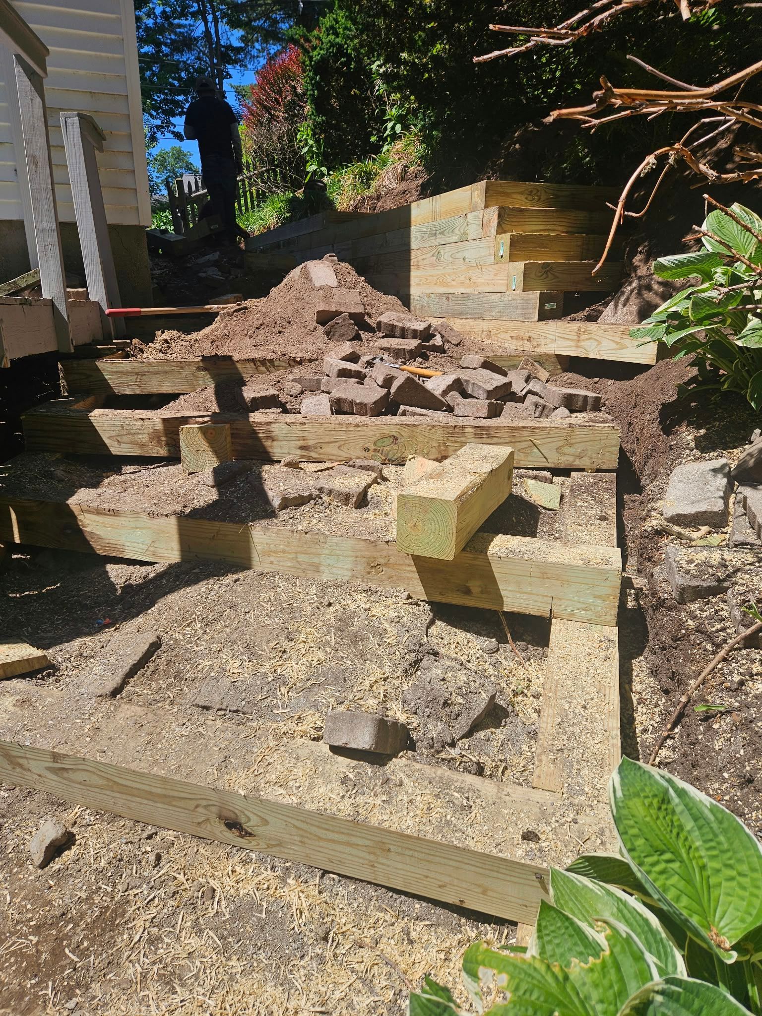 Stone steps and retaining walls in a sunlit garden, covered with dirt and debris after a collapse.