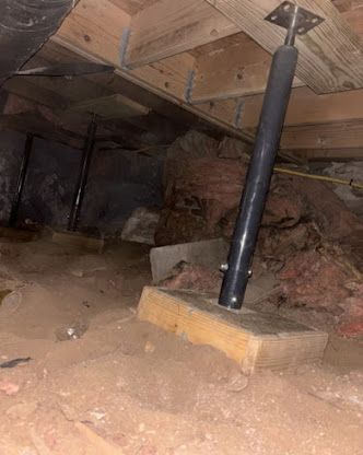 Crawlspace with dirt floor, exposed insulation, and a black adjustable steel support jack under a wooden beam.