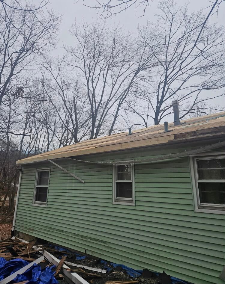 Green house siding with damaged roof under bare trees, debris piled along the side