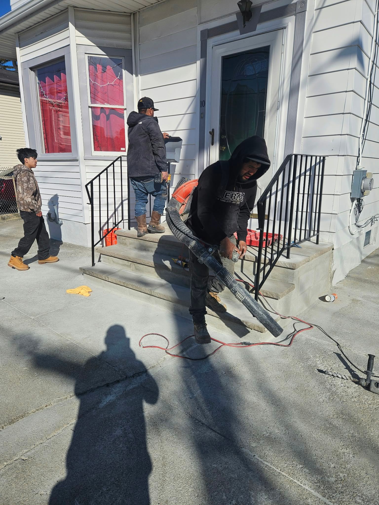People shoveling snow on a front porch and walkway outside a house.