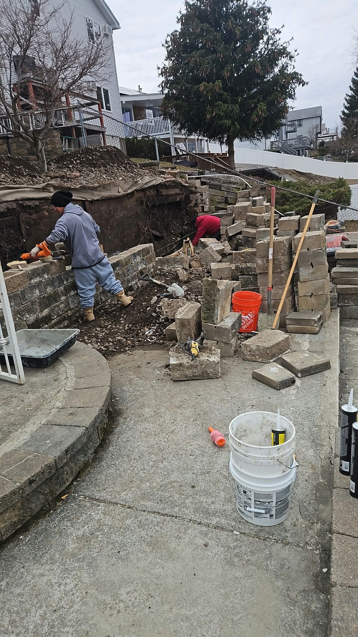 Workers and tools at a residential garden excavation site with stone retaining walls and gravel path