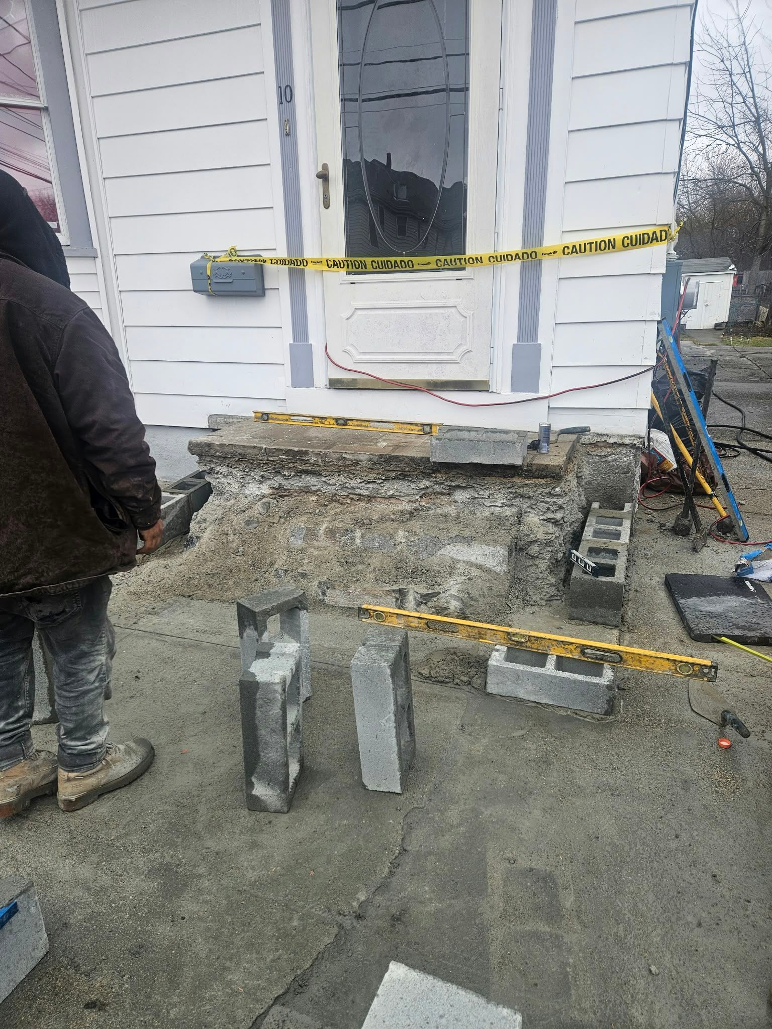 House entry under construction with broken concrete steps, caution tape, and workers nearby