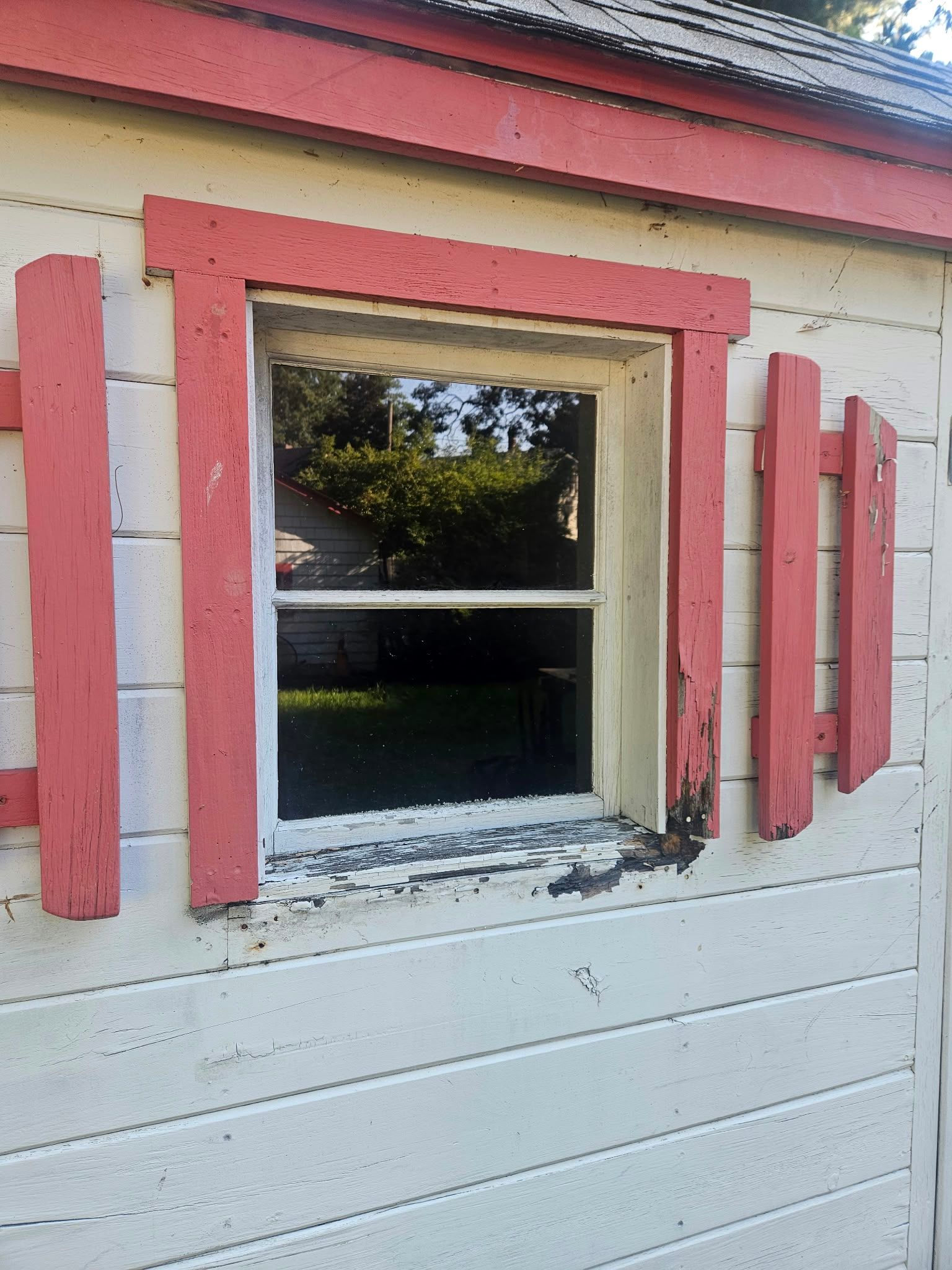 Red-trimmed window on a white building with open shutters and chipped paint.