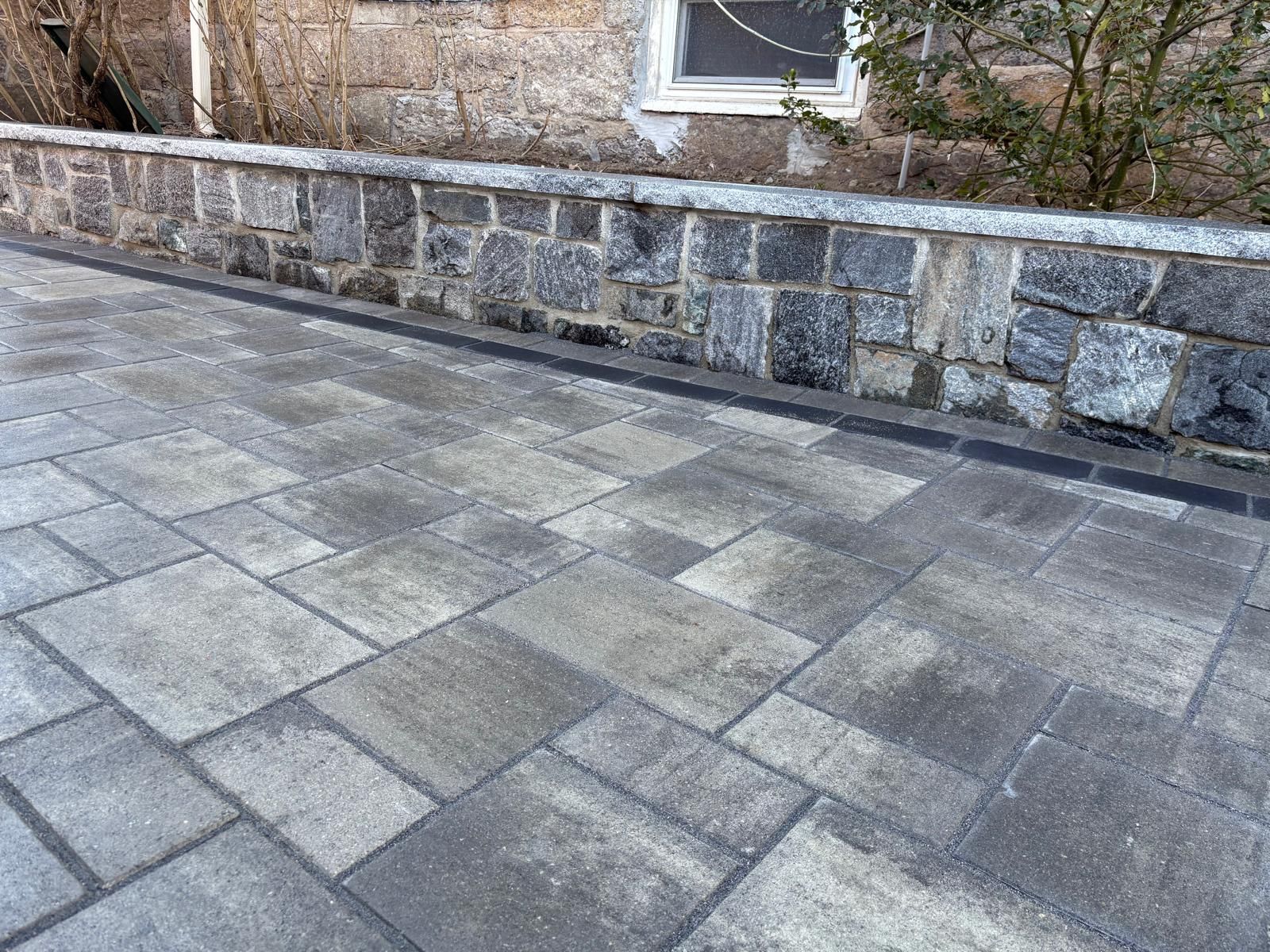 Stone patio with large gray pavers beside a low stone wall and building window