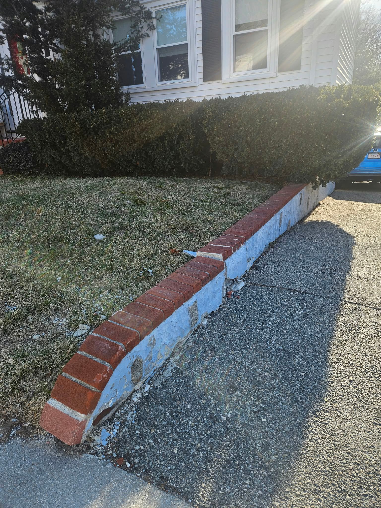 Curved brick-edged retaining wall beside a gravel driveway and grassy slope in front of a house
