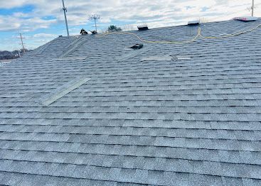 Gray shingled roof with several vents under a clear blue sky