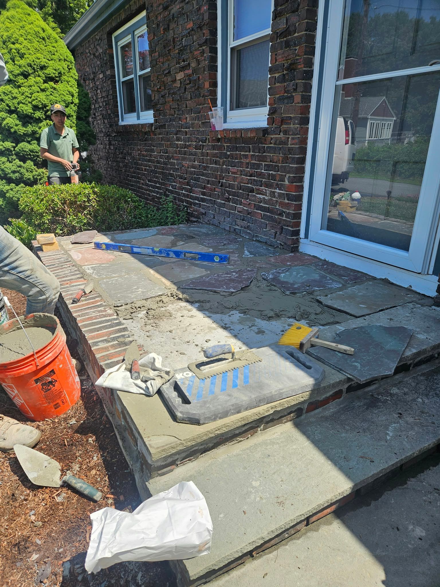 Side patio renovation with brick house wall, concrete steps, tools, and a white sliding door