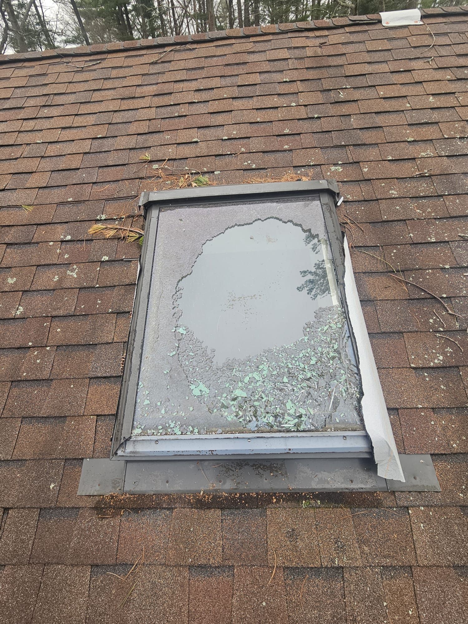 Damaged skylight on a shingled roof, with cracked glass and peeling sealant.